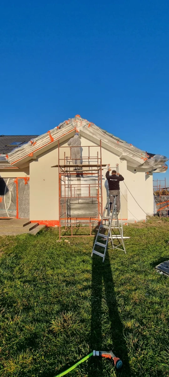 Malowanie elewacji domu zewnętrznej na rusztowaniu przez pracownika